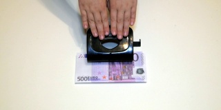 慢慢的特写，手压在钞票上的小孔上，里面有500欧元，钱