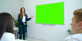 年轻快乐的老师在教室里用一块绿色的屏幕板子教学生