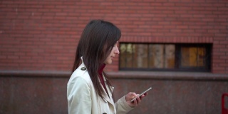 年轻女子拿着智能手机在城市里行走，用稳定器拍摄。侧视图