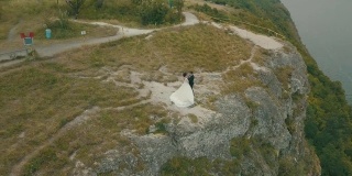 年轻美丽的新婚夫妇一起在海边山上的斜坡上。可爱的新郎和新娘。从空中射击。空中拍摄