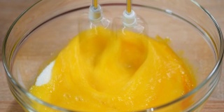 近距离女性的手打蛋黄与糖在一个玻璃碗在一个木制的背景桌子。
