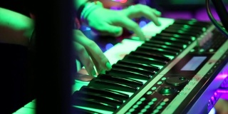 在彩色舞台灯光下弹奏电子钢琴的女性手，特写。