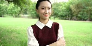 年轻迷人的亚洲女人微笑与双臂交叉在校服在公园户外