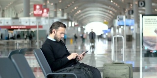 乘客在机场候机室边听音乐边使用智能手机