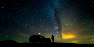 一个男人和一个女人站在一辆汽车旁，映衬着星空。时间流逝