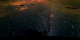 在星空背景下，一个男人和一个女人站在一辆汽车旁。时间流逝