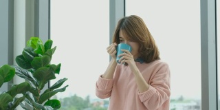 年轻美丽的亚洲女人喝咖啡，透过窗户与城市的看法与幸福，人们的生活方式