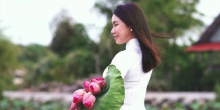 美丽的越南女子手持粉色莲花，在大莲花湖的木桥上呼吸新鲜空气，越南，亚洲或东南亚旅游概念