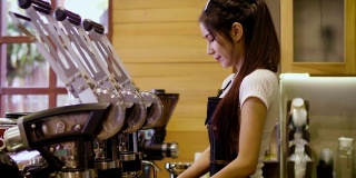 年轻微笑的亚洲女性咖啡师或女性咖啡所有者使用咖啡机，并在咖啡店咖啡厅看着镜头