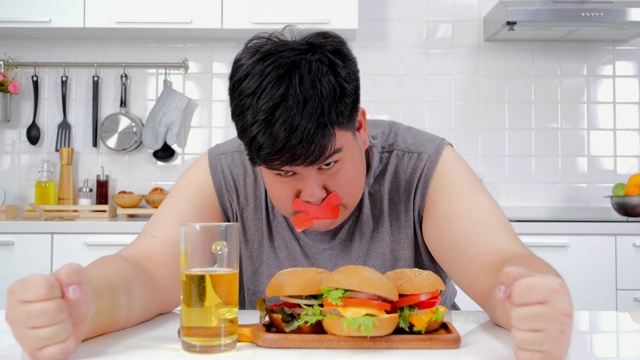 年轻失意的男子用卷尺绕着嘴巴定形垃圾食品。一个有负罪感的节食者。饮食限制应激概念。真实的身体