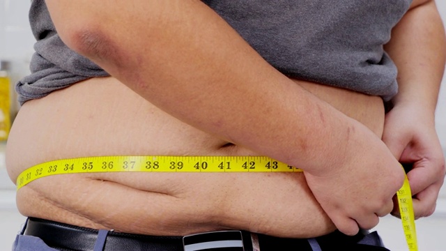 超重男子用卷尺检查自己超重。健康的概念。真实的身体