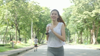 年轻迷人的女人在绿色城市公园跑步锻炼户外健身跟踪可穿戴技术。健身跑步运动的人与健康的生活理念。视频素材模板下载
