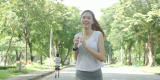 年轻迷人的女人在绿色城市公园跑步锻炼户外健身跟踪可穿戴技术。健身跑步运动的人与健康的生活理念。