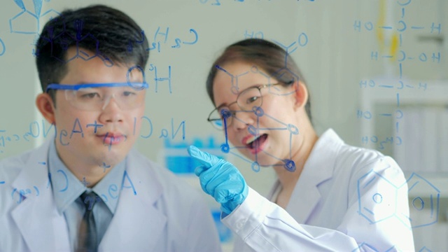 科学实验室:在生命科学实验室工作的保健研究人员。年轻的男性和年轻的女性化学家自信地在透明的板上绘制配方
