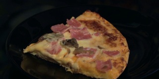 特写一片披萨与火腿，蘑菇，奶酪在一个黑色的盘子
