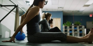 一群20多岁的女性在健身室里靠在健身球上，双手伸出，同时脉搏跳动