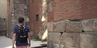 夏日里，一个年轻人正沿着古老的中世纪建筑墙走着