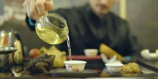 师傅将绿茶从玻璃茶壶中倒进白杯子里