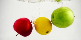 苹果、柠檬和橘子在慢镜头中冒着气泡掉进水里。果实上孤立白色背景。