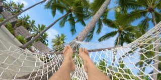 POV:放松的人在美丽的棕榈树下的吊床荡秋千