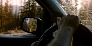 美丽的特写镜头，两个男性的手握着汽车方向盘驾驶在约塞米蒂森林道路上的慢动作。