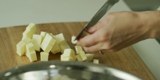 一个年轻女人的手用一把大菜刀把黄油切成小块，拿起黄油，撒在一个金属搅拌碗里的面粉上