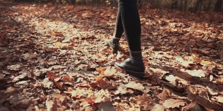 女性的脚在秋天的林地里行走的特写背影