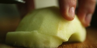 一个女人的手切一个削皮和减半的苹果用一把厨房刀