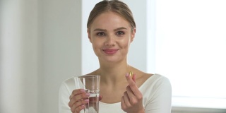 在白色的室内，一个女人在吃药，从玻璃里喝水