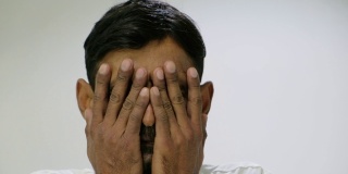 一名留着胡茬的印度男子看着镜头，在悲伤、绝望和痛苦中把手放在脸上
