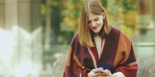 一名年轻女子在秋天的公园里用智能手机发短信
