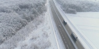 卡车和汽车在被积雪覆盖的田野和森林包围的高速公路上行驶