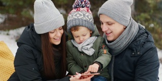 在冬天的森林里，一家人带着儿子看手机上的照片。快乐的圣诞节