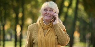 微笑的老妇人在公园里用手机聊天，还有家人和朋友