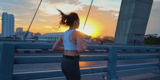 日落，年轻女子慢跑过桥的慢镜头