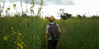 快乐快乐的男游客背包客带着帽子和包兴奋地在乡村草原上行走跳跃