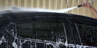 慢动作工人在洗车服务中使用高压水射流清洗黑色汽车。