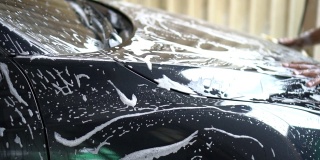 洗车服务的慢动作工人用海绵清洗一辆黑色汽车。