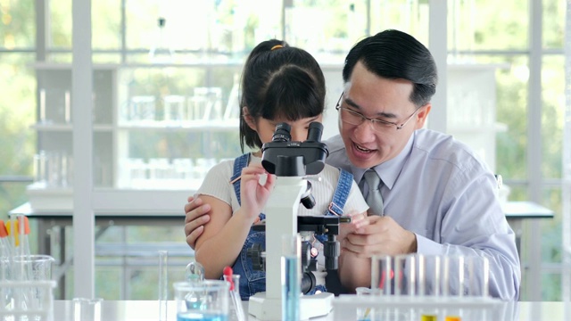 亚洲小孩和老师在学校实验室用显微镜观察。小女孩用显微镜学习科学课。教育的主题