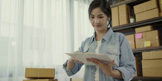 美丽聪明的亚洲年轻企业家女企业家企业主中小企业检查产品在股票和写在剪贴板在家里工作。小企业主在家办公的概念。