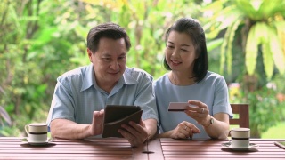成熟的成年夫妇在网上购物的数字平板电脑和信用卡在阳台后院的早晨。视频素材模板下载