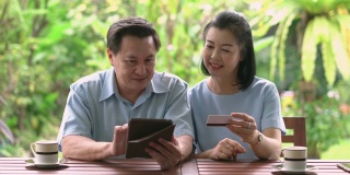 成熟的成年夫妇在网上购物的数字平板电脑和信用卡在阳台后院的早晨。