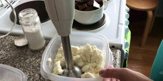 一个女人在一个容器里用搅拌机磨白软干酪。配料甜点。