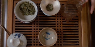 师傅从盖湾的茶壶里倒热水，茶几上放绿茶
