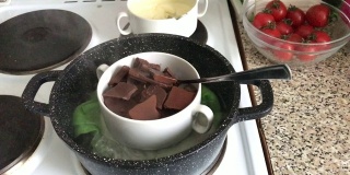 把黑巧克力和白巧克力放在炉子上的碗里。巧克力在水浴中融化成为一种甜点。