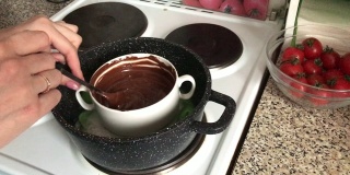 在盘子里搅拌黑巧克力的女人。巧克力在水浴中融化成为一种甜点。