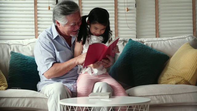 快乐的小女孩和爷爷在家里读故事书。香港的家庭