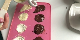 一个女人用融化的巧克力把凝乳填在硅胶里。做甜点。