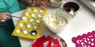 这位女士将凝乳填充物放入硅胶模具，涂上融化的白巧克力和黑巧克力。做甜点。