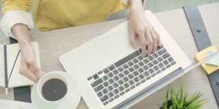 美丽的年轻微笑的亚洲女人工作在笔记本电脑和喝咖啡在家里的客厅。亚洲商业女性工作文件财务和计算器在她的家庭办公室。享受在家的时光。
